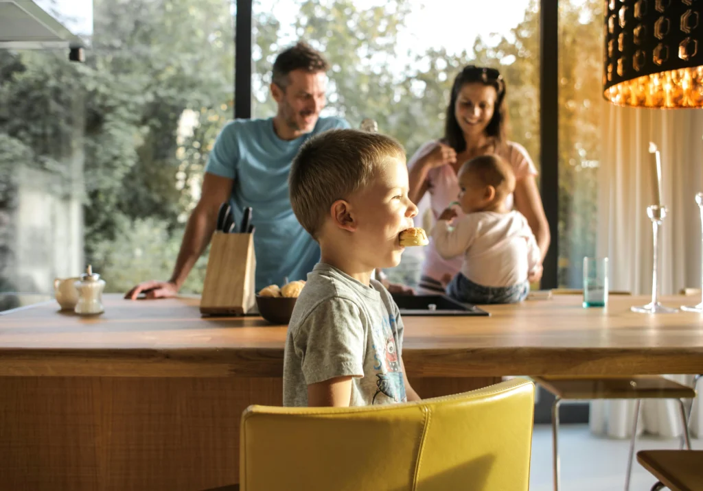A happy family enjoying breakfast in a modern, well-lit kitchen with large windows that allow natural light to flood in, embodying the principles of Vastu Shastra for creating a harmonious living space.