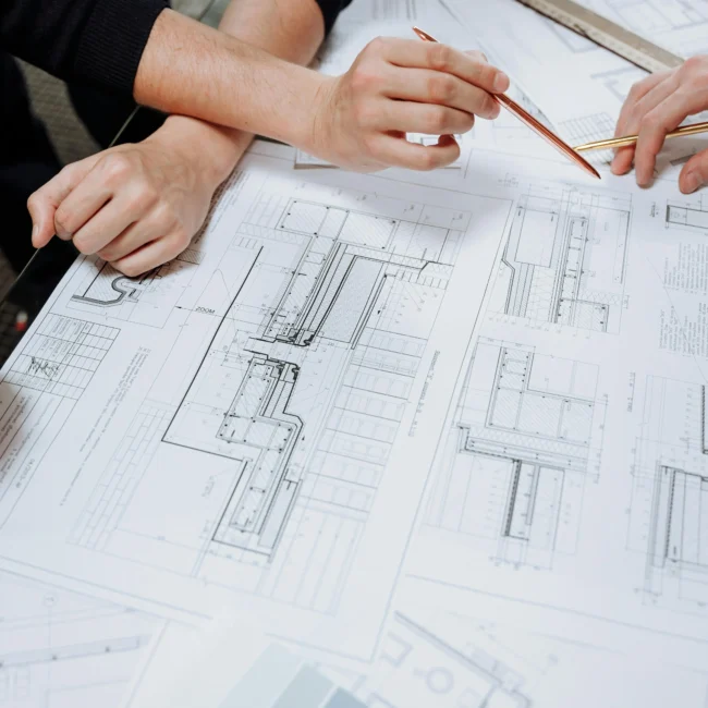 Close-up of architects' hands working on detailed blueprints and design plans, emphasizing the integration of Vastu Shastra in modern architectural projects to ensure balanced and auspicious designs.