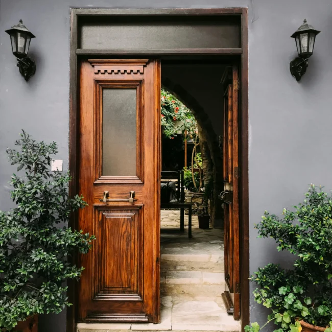 An inviting wooden front door flanked by green plants, leading to a cozy home interior. This design reflects Vastu Shastra principles, promoting positive energy and welcoming vibes.